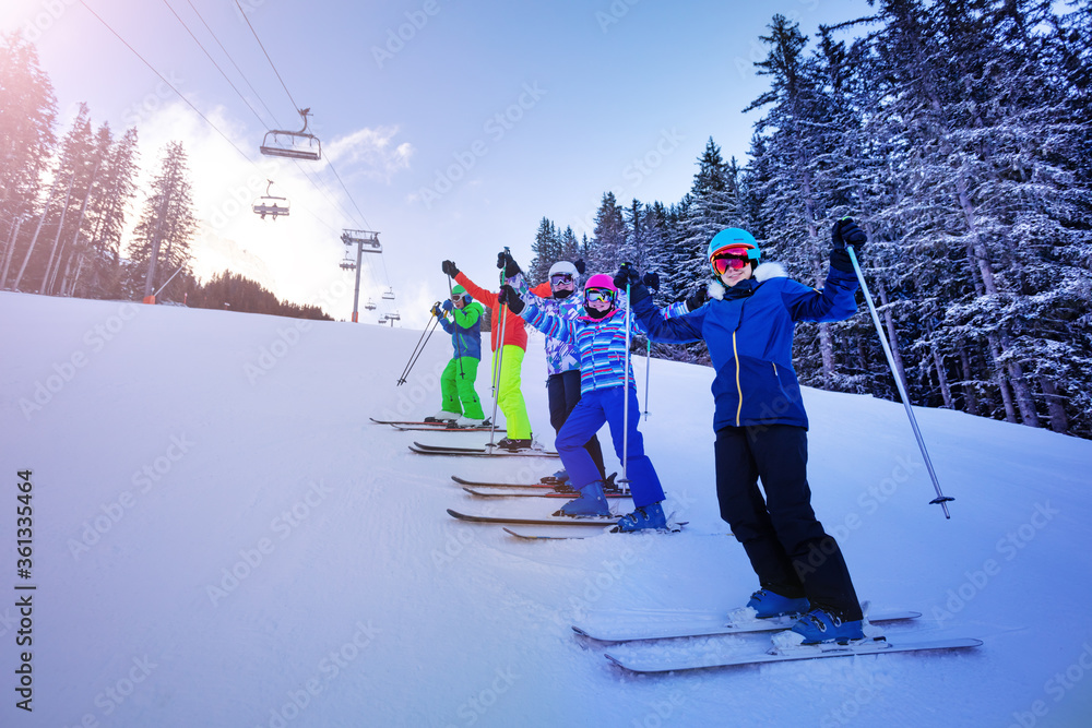 滑雪学校的一群孩子排成一行站在斜坡上，开心地举起双手