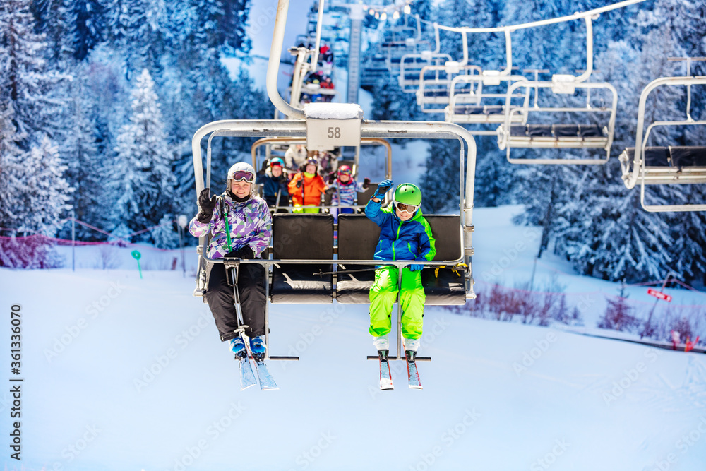 一群孩子坐在山地滑雪场的升降椅上挥手