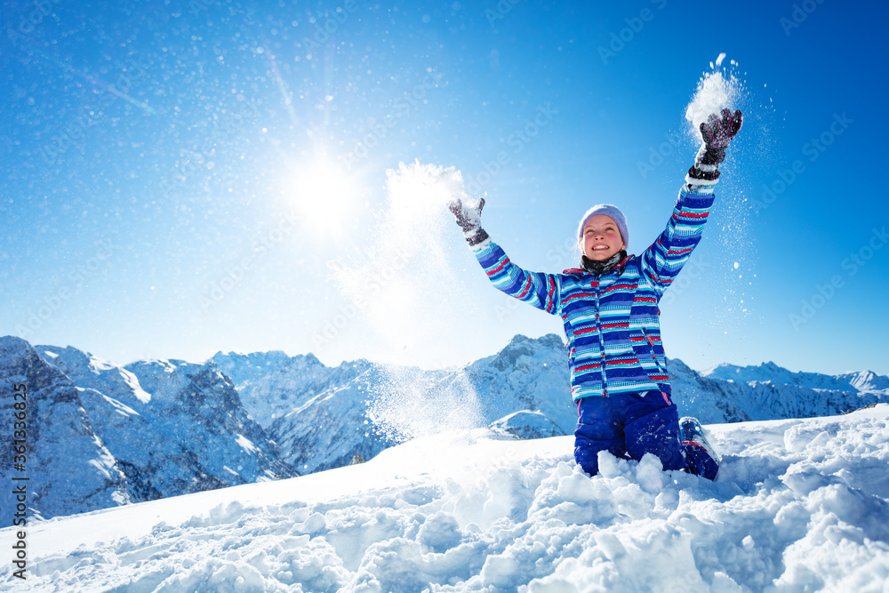 美丽的笑着微笑的女孩将雪抛向空中，在蓝天和群山上特写