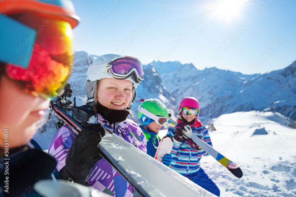 Portrait of a girl in the mountains hold ski on the shoulder stand on snow mountain top in a group o