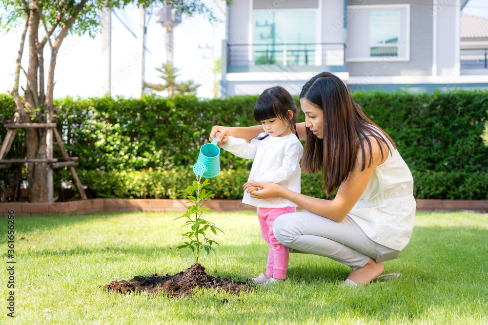 Asian family mother and kid daughter plant sapling tree and watering outdoors in nature spring for r