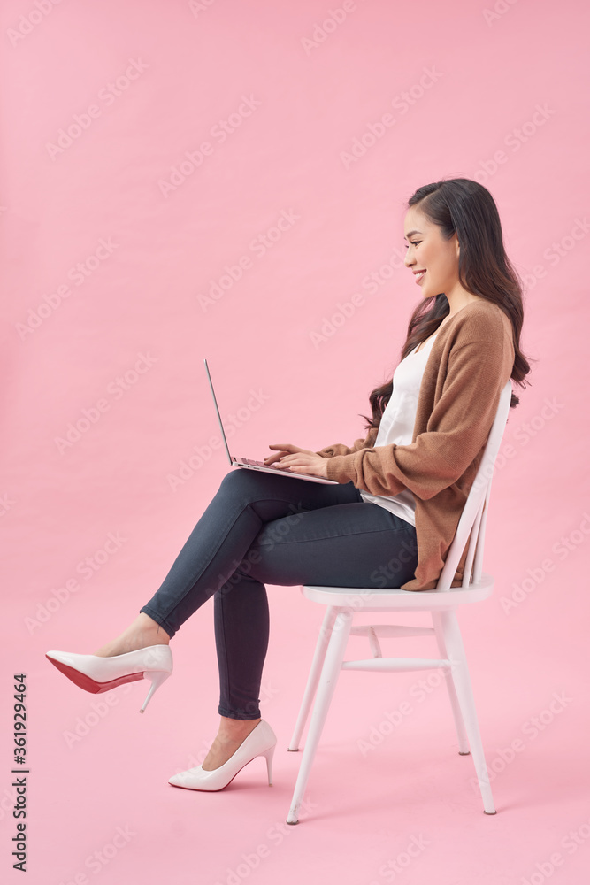 美丽快乐的女人，拿着笔记本电脑工作，在粉色背景下与世隔绝