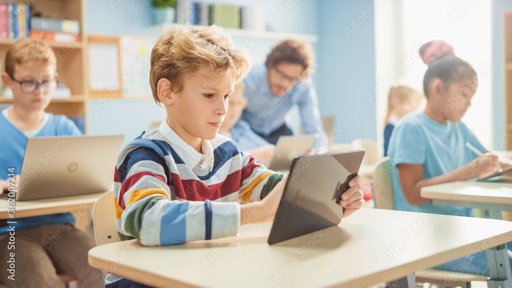 小学计算机科学课：聪明男孩使用数字平板电脑，他的同学担心