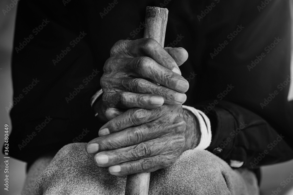 一位亚洲老人双手拄着拐杖坐着。