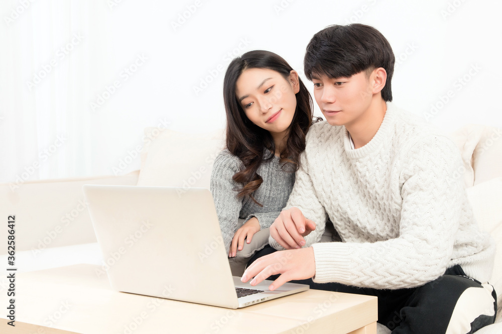 冬天，一对亲密的亚洲年轻情侣坐在沙发上，开心地玩电脑
