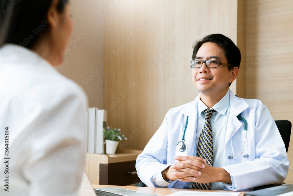 医生和病人坐在医院窗户附近的诊所桌子旁交谈。医生