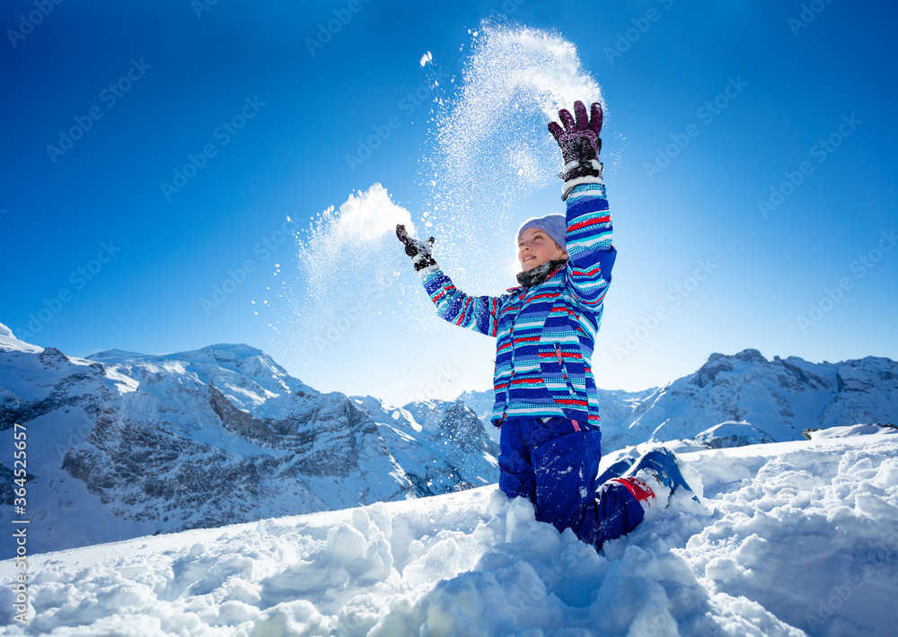 滑雪女孩跪在山顶上向空中扔雪的近景肖像