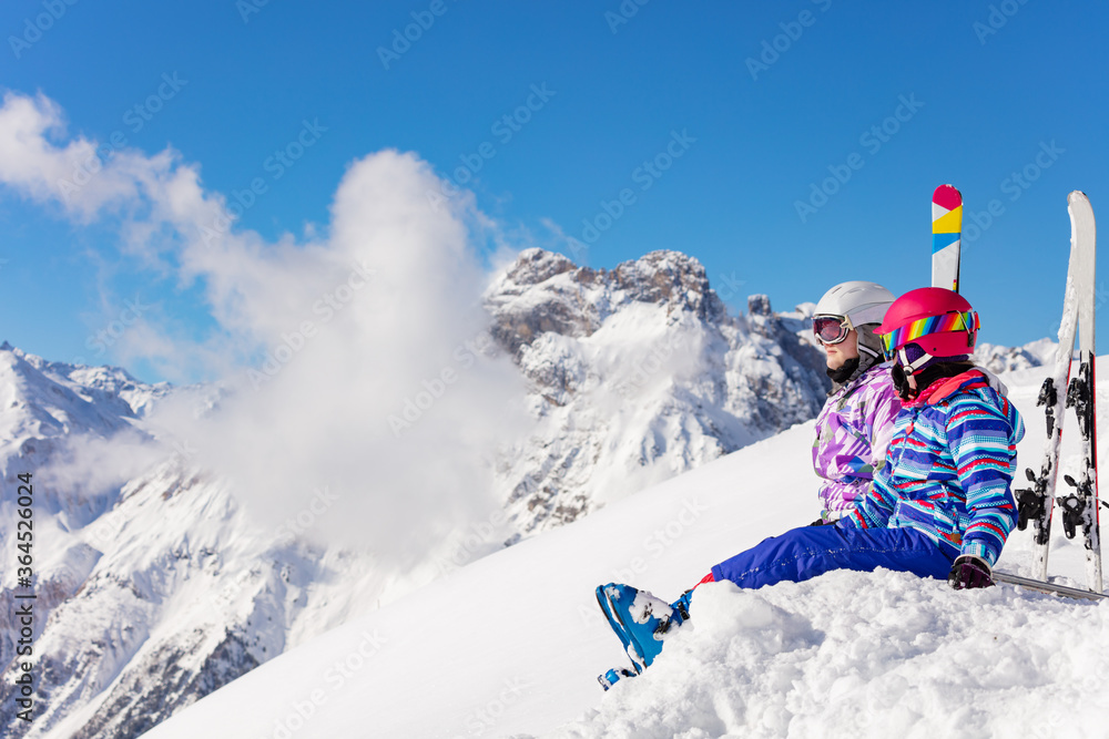 两个快乐的女孩坐在山上，滑雪翻越高峰，雪中云看山谷