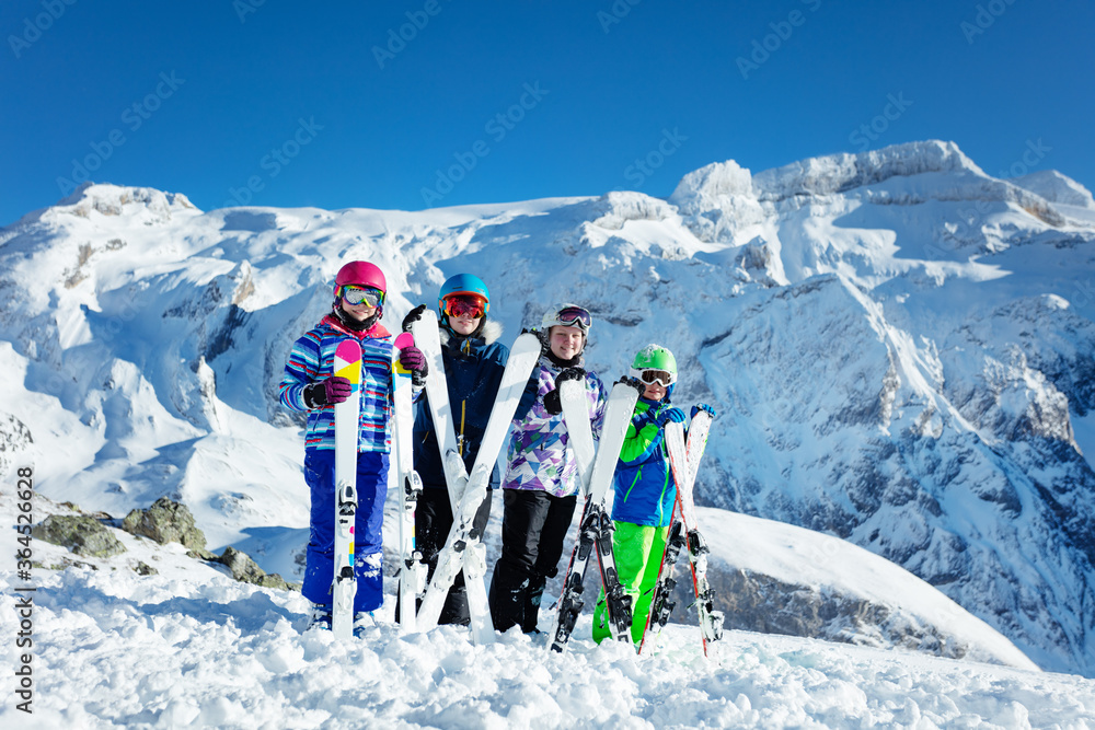 滑雪学校团体概念-四个快乐的孩子站在他们面前，手里拿着设备，靠着微笑