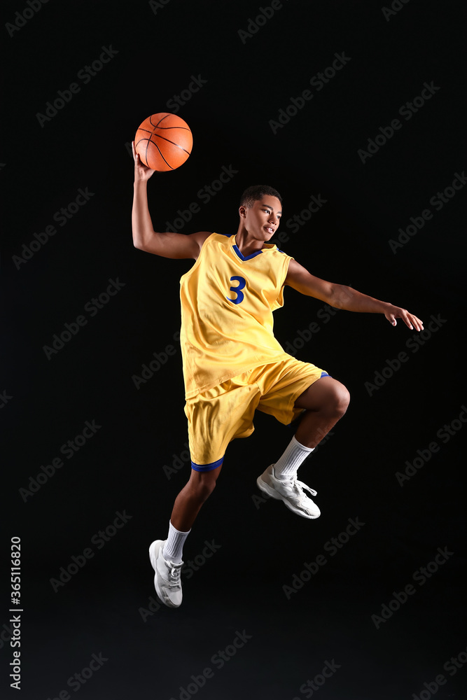 黑暗背景下的年轻跳跃非裔美国篮球运动员