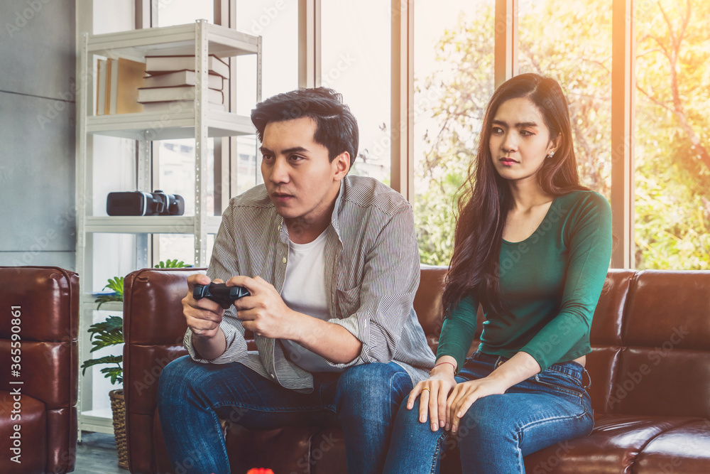 一对年轻的亚洲夫妇沉迷于电脑游戏。家庭问题概念。
