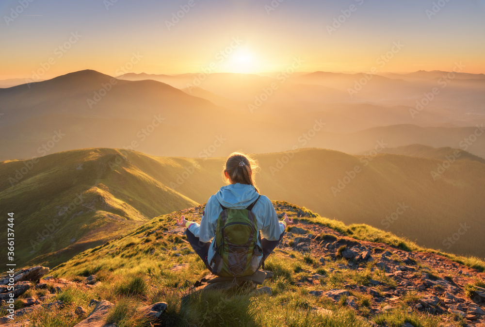 Young woman with backpack sitting on the mountain peak and beautiful mountains in fog at sunset in s