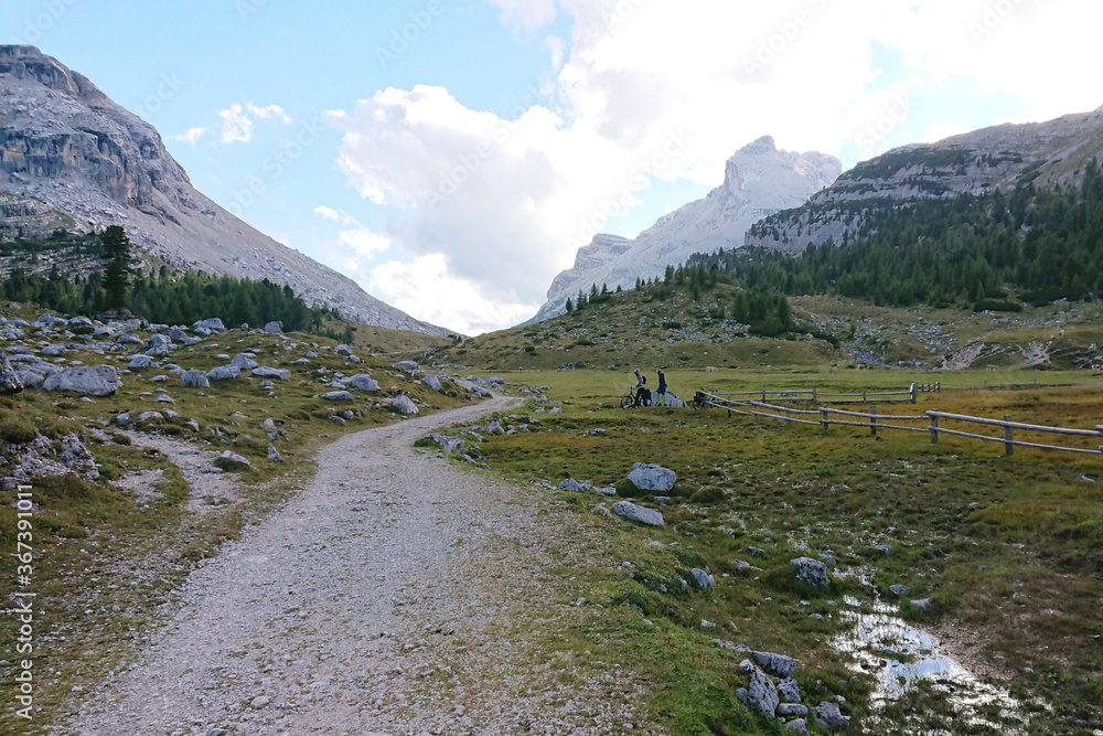 意大利北部的白云石景观。一条灰色的道路穿过一个绿色的山谷，一直延伸到地平线。