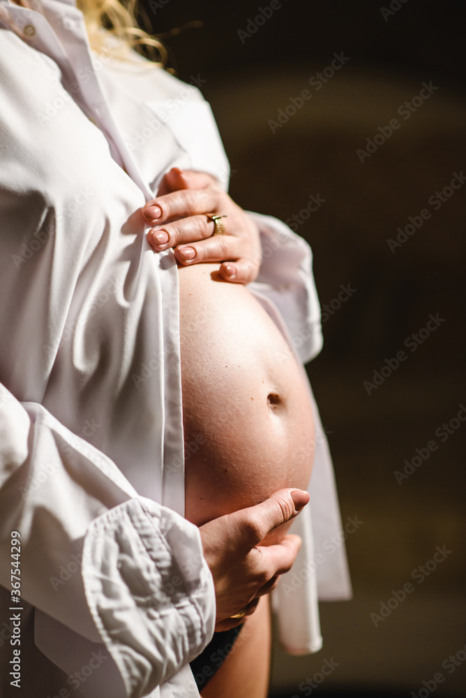 穿着白衬衫的孕妇用手抱着肚子