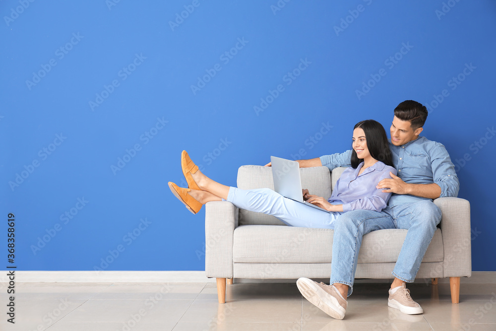 年轻夫妇带着笔记本电脑在家的沙发上放松