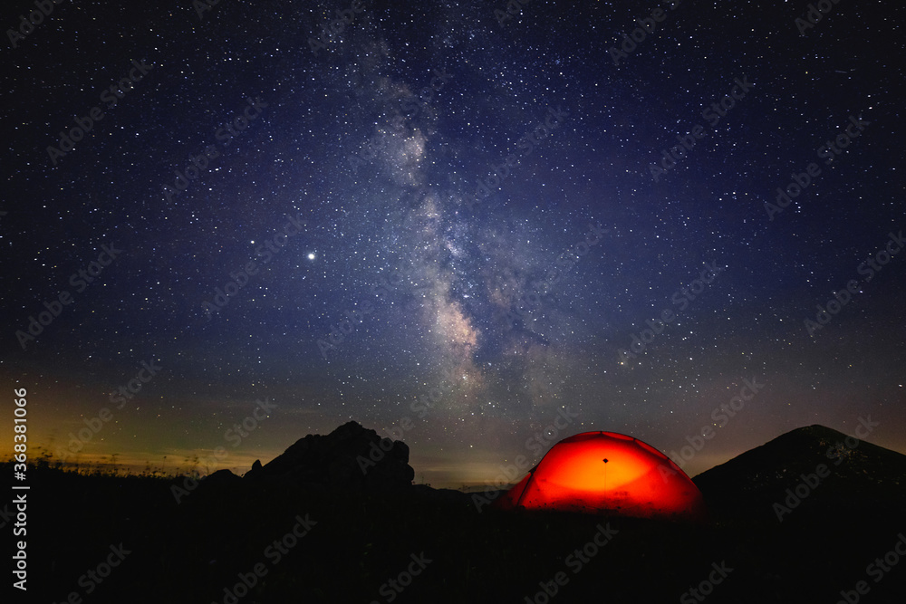 美丽星空下的橙色帐篷在夜晚闪闪发光。银河系下的橙色小屋a