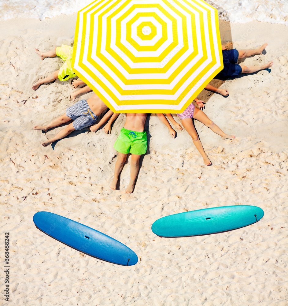 一群孩子躺在沙滩上，打着大太阳伞，旁边有冲浪板，从上面看