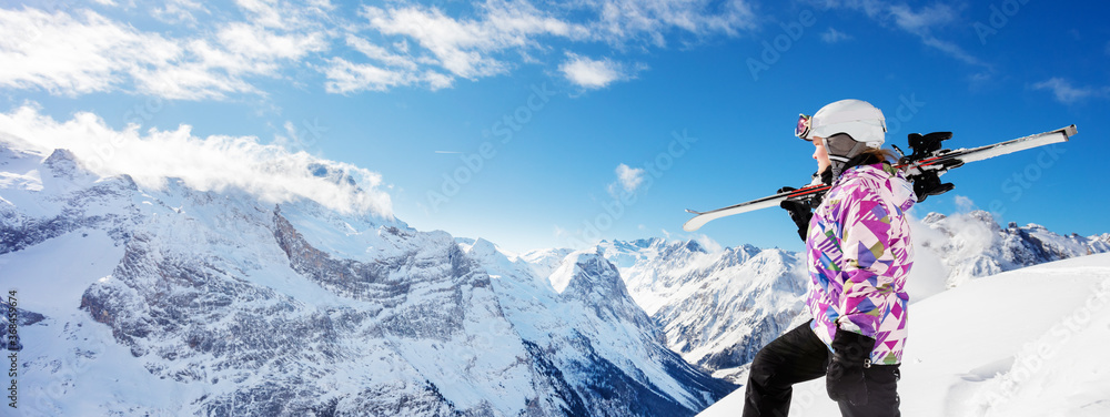 青少年女孩滑雪运动员在山顶上的侧视图，将滑雪板放在肩膀上越过山峰。
