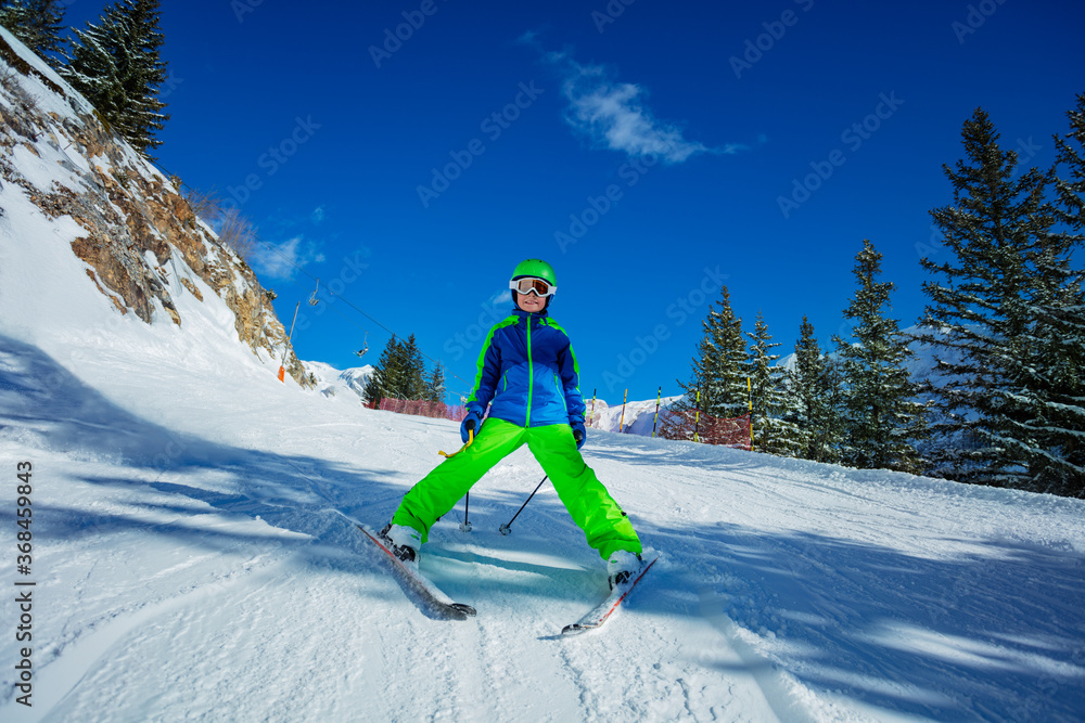 Cute 10 years old boy skier learning to ski down the slope in bright green outfit on sunny day