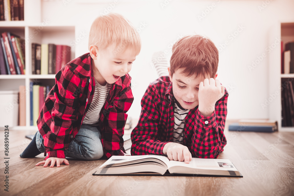 三岁的孩子和他的哥哥坐在家里的书中间