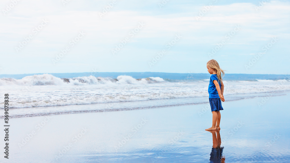 孩子站在黑沙滩上。梦想中的孩子看着海浪景观，打破风暴波
