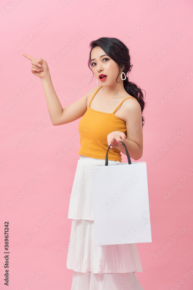 一位年轻的亚洲女性拿着购物袋的肖像，被隔离在粉红色的背景上。