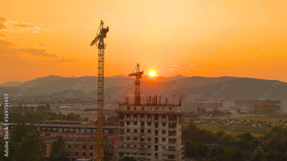 DRONE: Two cranes stand near an apartment building under construction at sunrise