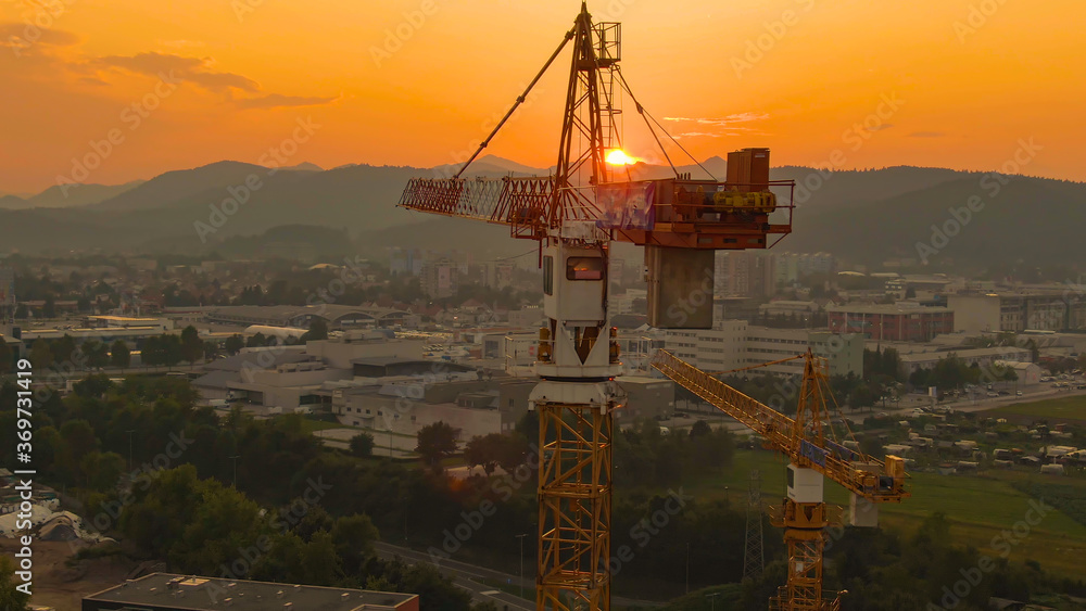 AERIAL: Flying around two towering cranes illuminated the golden evening sun