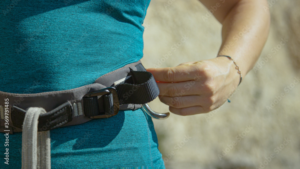 CLOSE UP: Woman fastens the harness around her waist before climbing a cliff.