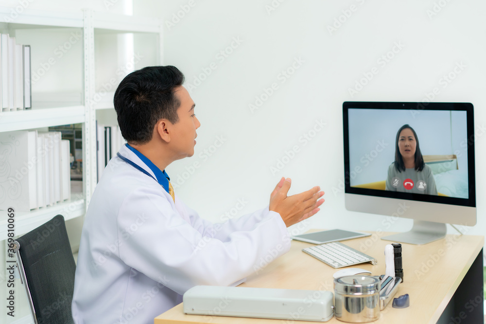亚洲男医生穿着白大褂，戴着耳机，在笔记本电脑上使用视频会议