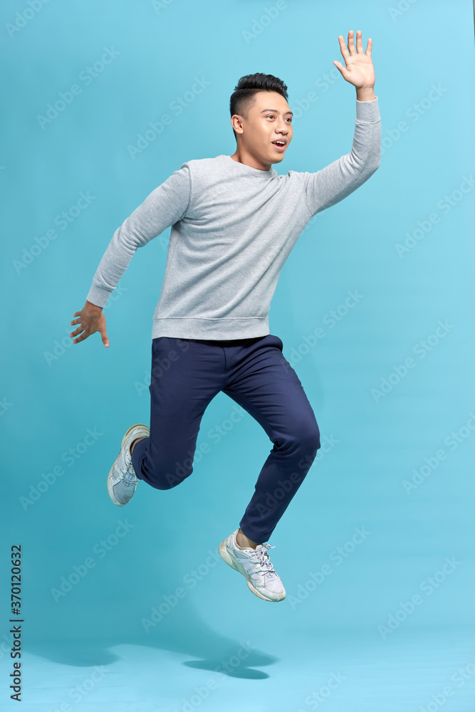 蓝色背景下，滑稽男子在空中奔跑或跳跃的全长照片