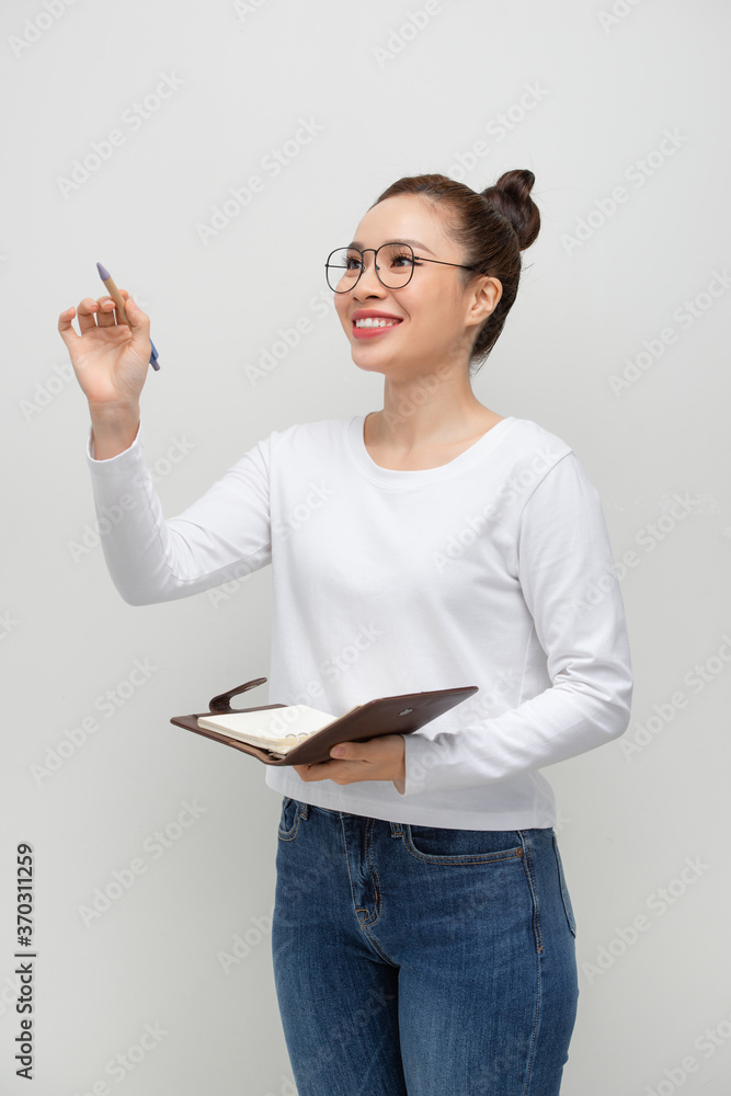 戴着眼镜的迷人年轻女子拿着打开的课本，对着隔离在白色b上的镜头微笑