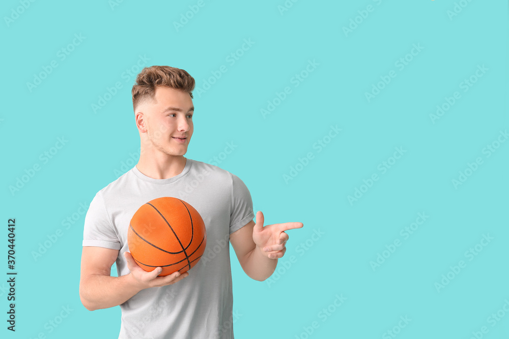 Young man with ball showing something on color background