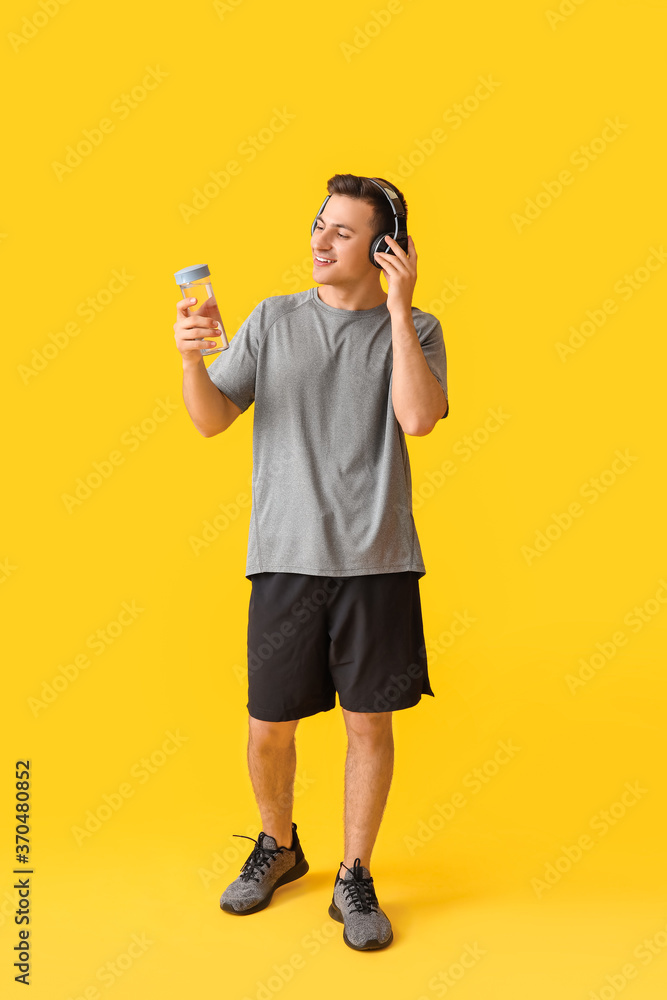 带着一瓶水和彩色背景耳机的运动型年轻人