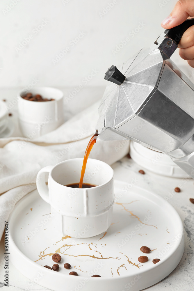 女人把热咖啡从锅里倒进桌子上的杯子里