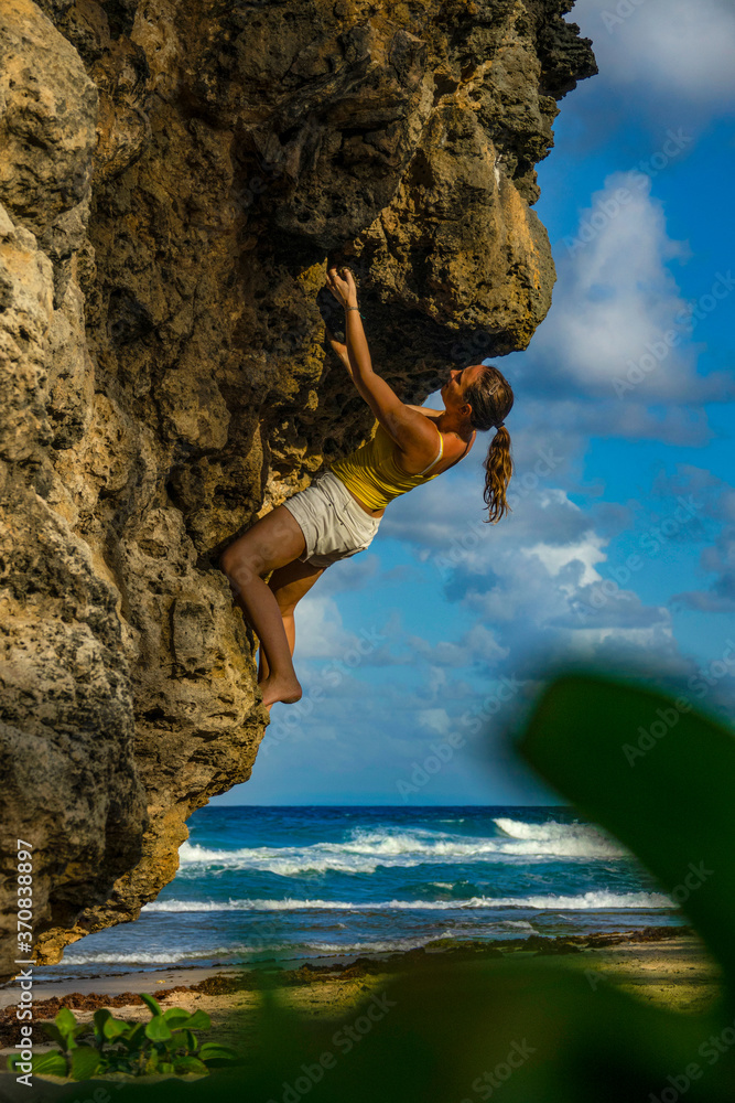 垂直：一名女性攀岩者在阳光明媚的夏日抱石的动作镜头。