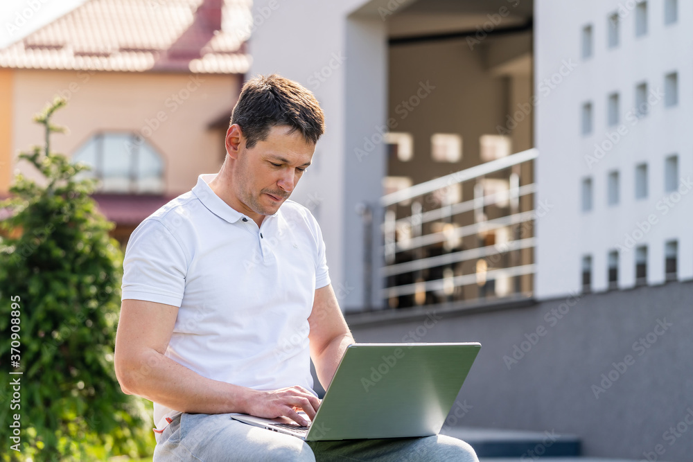 男人在笔记本电脑前工作。坐在房子附近的户外。自由职业。