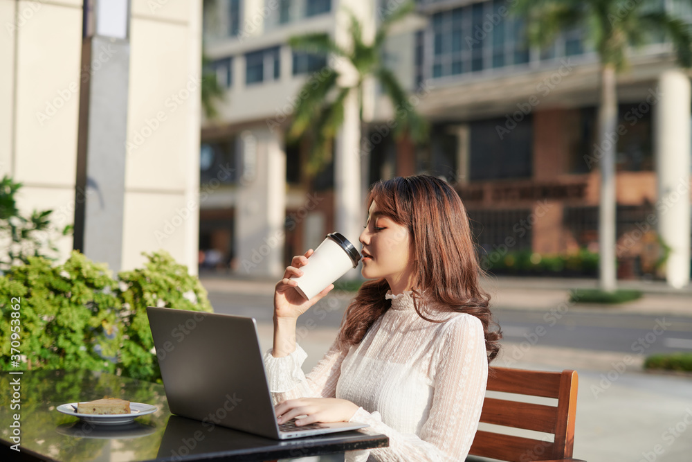 亚洲女商人坐在咖啡馆里，一边用笔记本电脑工作，一边在城市里放松。