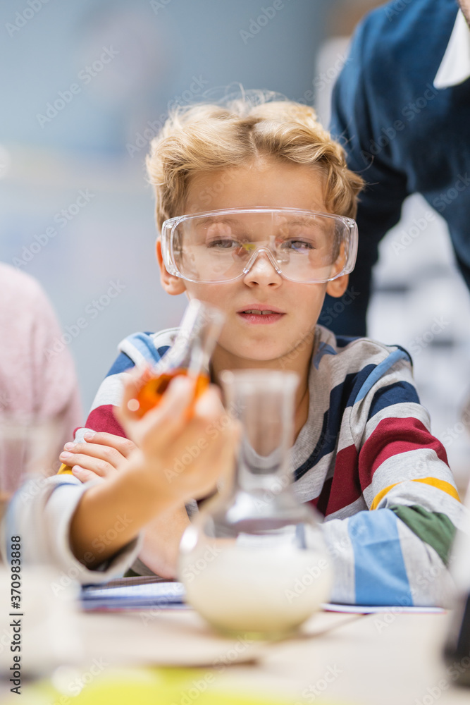 一个戴着安全眼镜的可爱小男孩在烧杯中混合化学品的肖像照片。小学