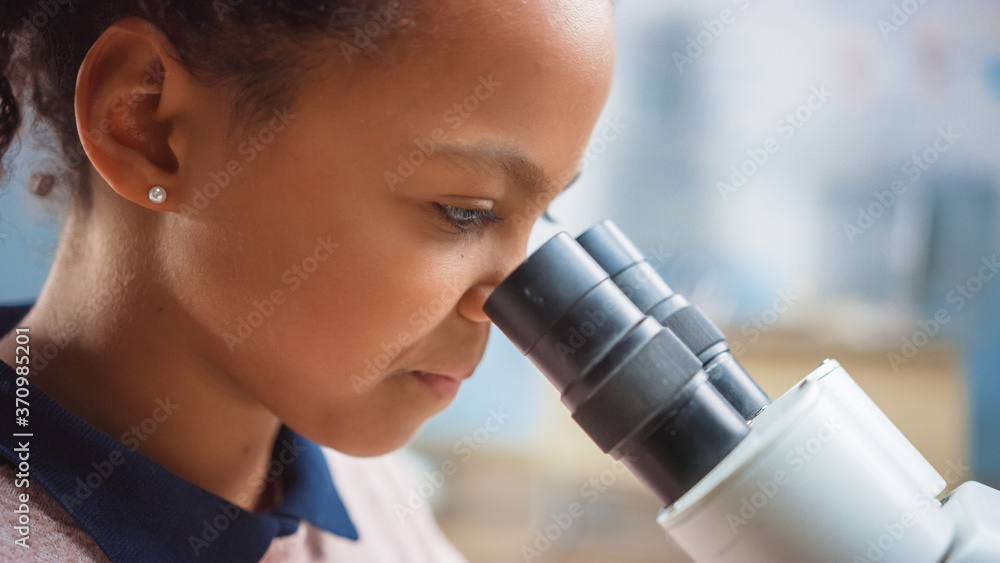 Portrait of Smart Little Schoolgirl Looking Under the Microscope. In Elementary School Classroom Cut