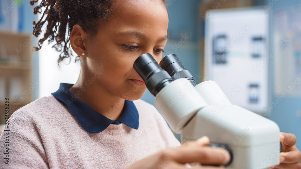 聪明的小女学生在显微镜下看的肖像。在小学课堂上剪