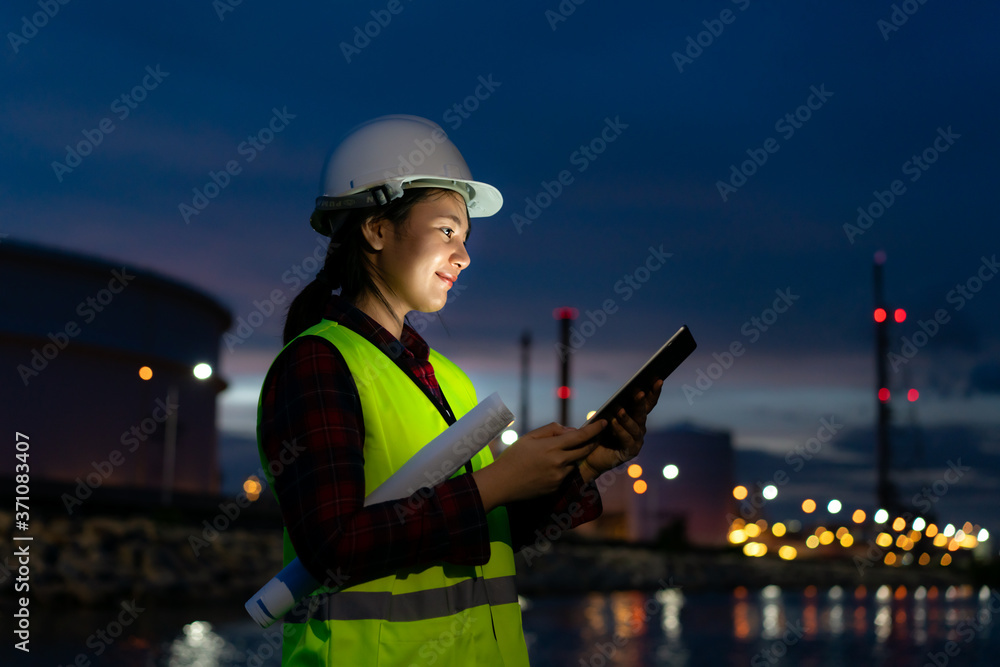 Asian woman petrochemical engineer working at night with digital tablet Inside oil and gas refinery 