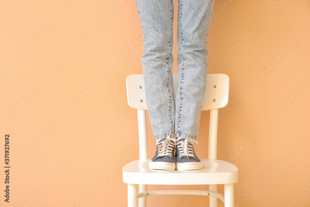 Beautiful young woman in jeans clothes on chair against color background