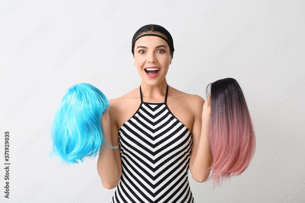 Beautiful young woman with different wigs on light background