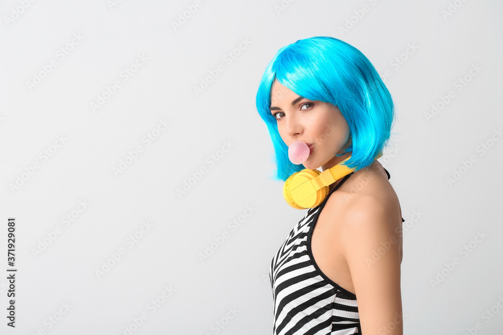Beautiful young woman in wig and with headphones on light background