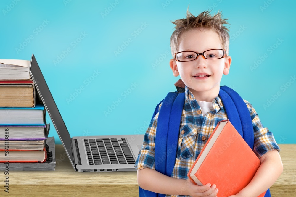 桌上放着笔记本电脑的一摞书和一个小学生