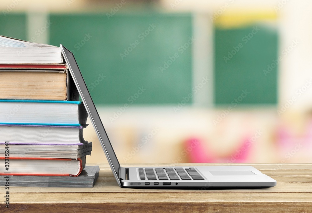 Stack of books with modern laptop on table
