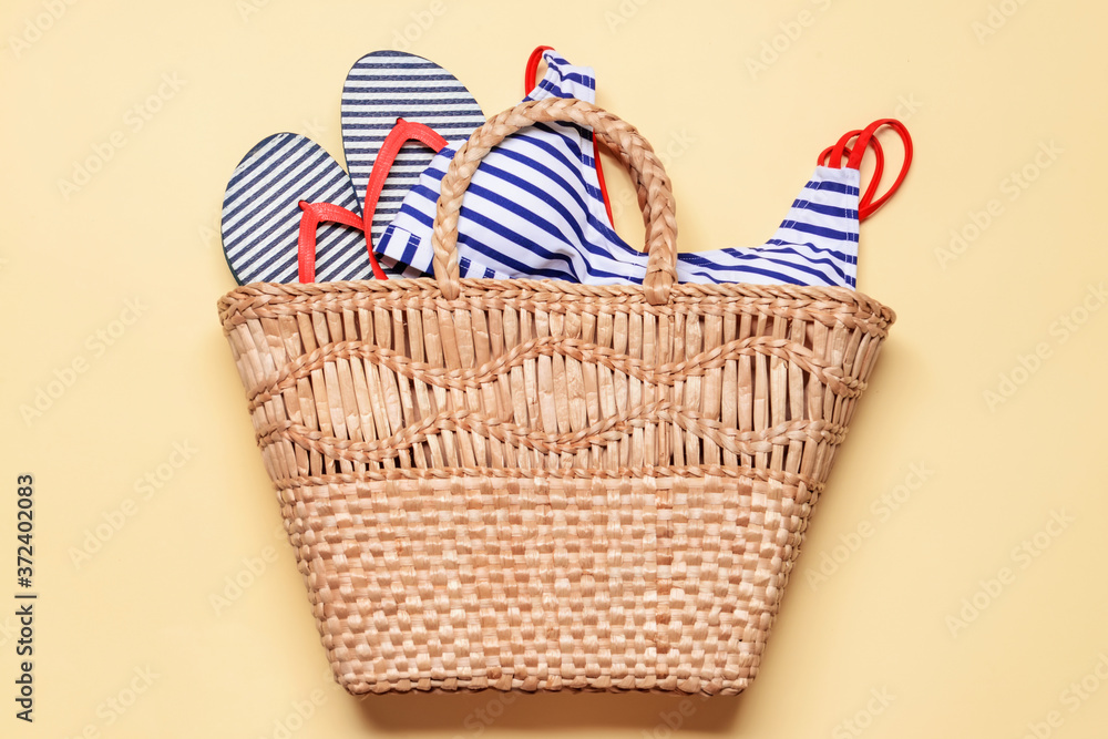 Straw bag with beach clothes on light background