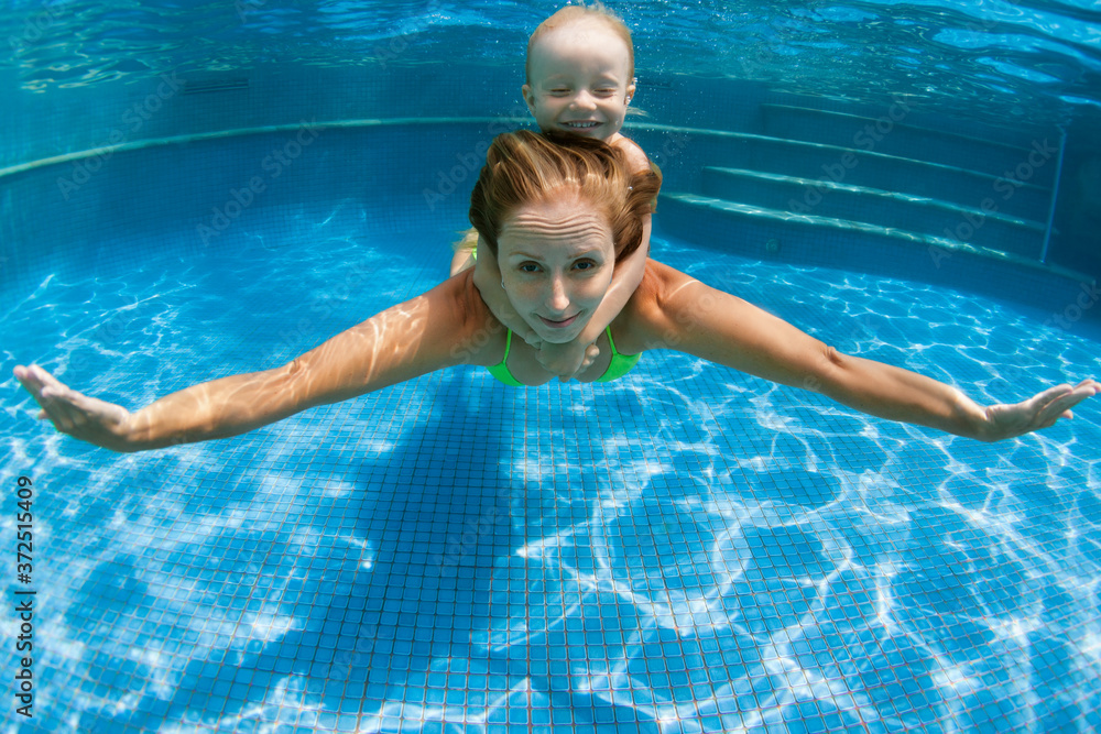 幸福的家庭-年轻的母亲，男婴学会游泳，在水下潜水。在游泳池里尽情跳跃