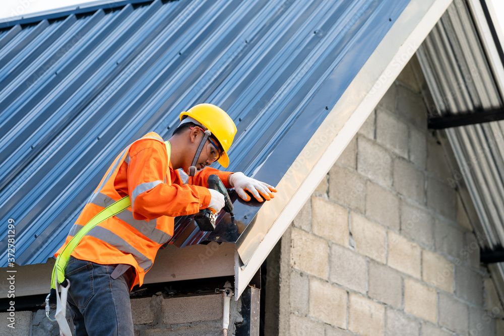 在新建筑屋顶上工作的屋顶工，在带金属板的新屋顶上使用电钻。